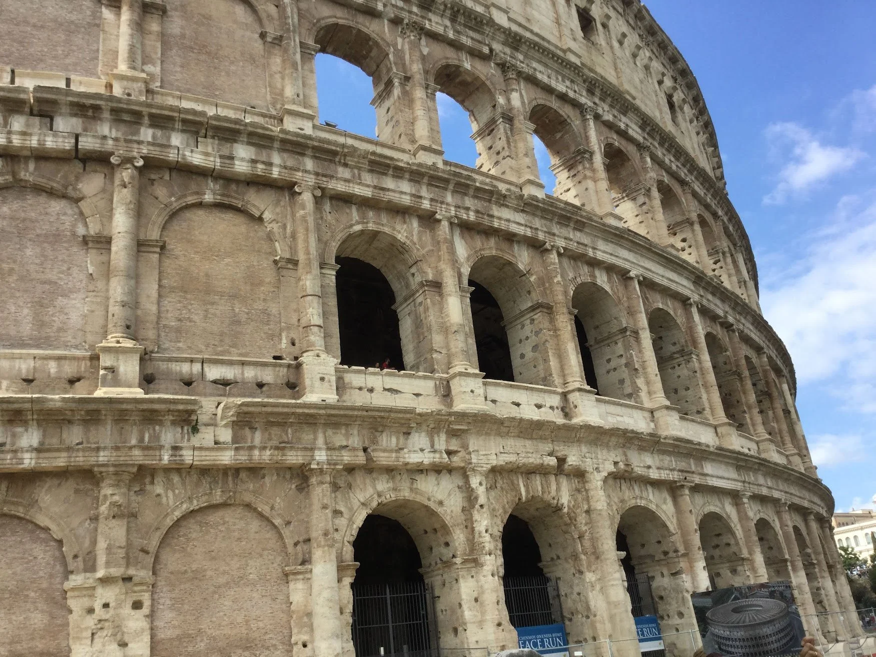 Close-up view of the exterior of the Roman Colosseum, showing its ancient stone arches and partial wall, with clear blue sky in the background.