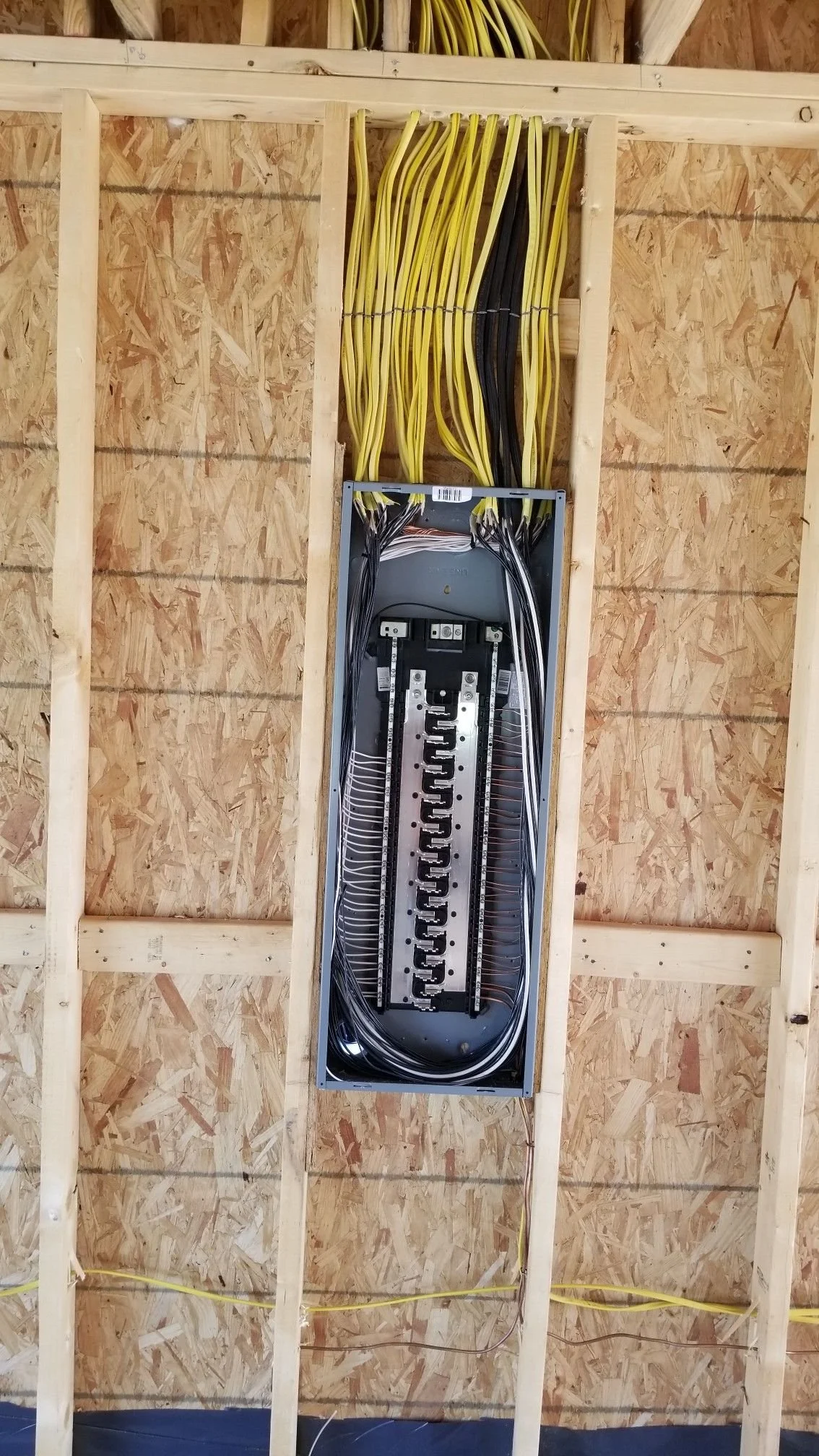 Electrical panel with multiple yellow and black cables installed on wooden framing of a building under construction.