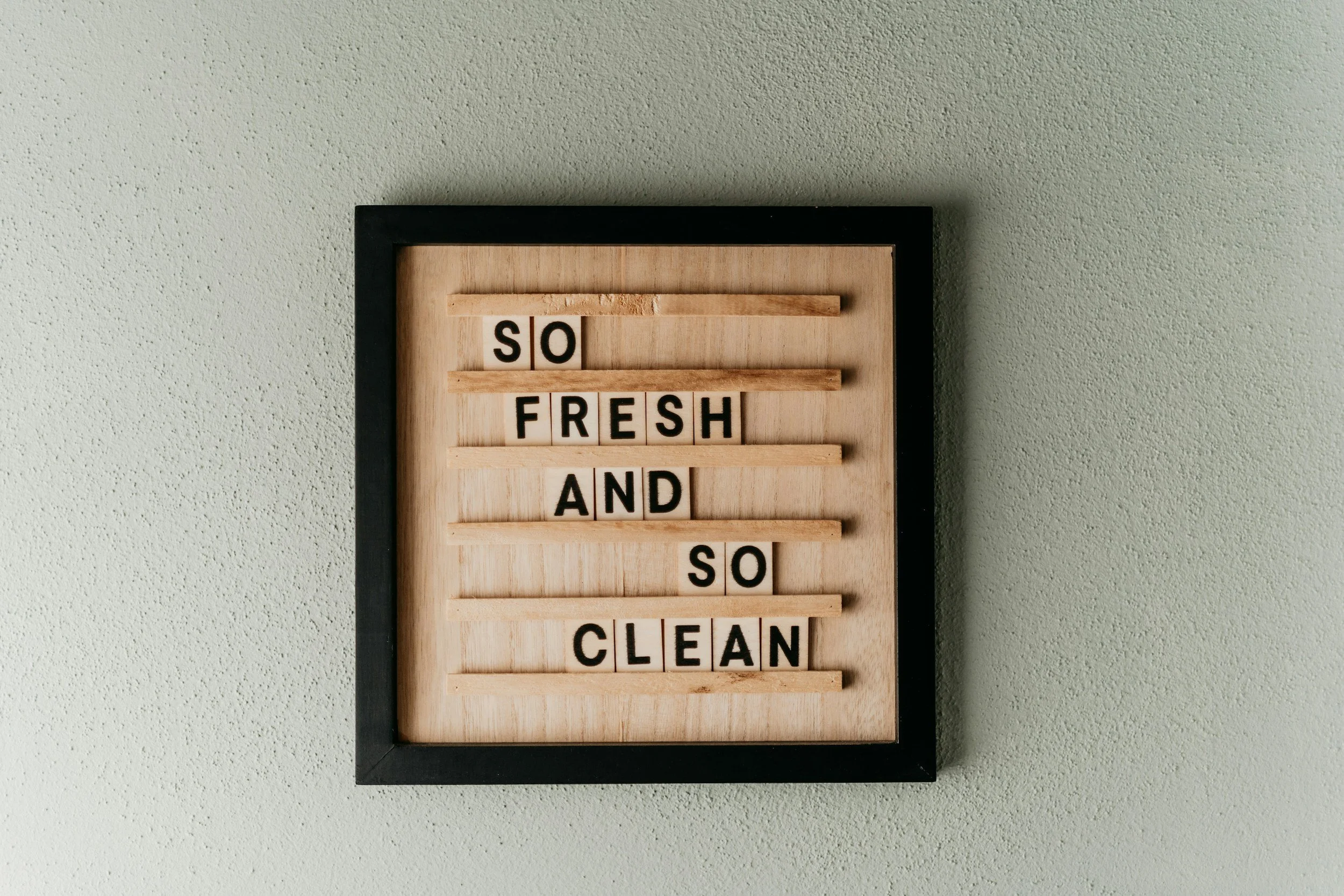 A message board with wooden slats spelling out 'SO FRESH AND SO CLEAN' on a light-colored wall.