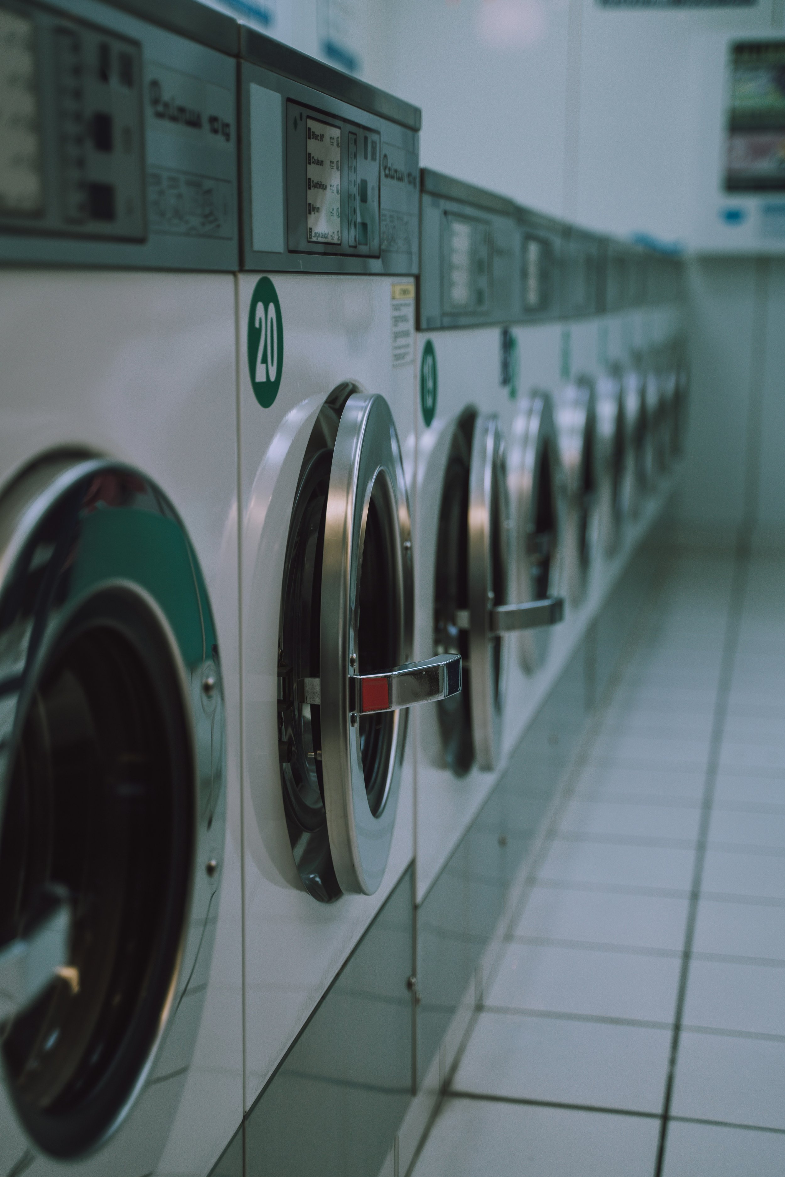 Row of silver laundry washing machines in a laundromat with round doors and control panels.