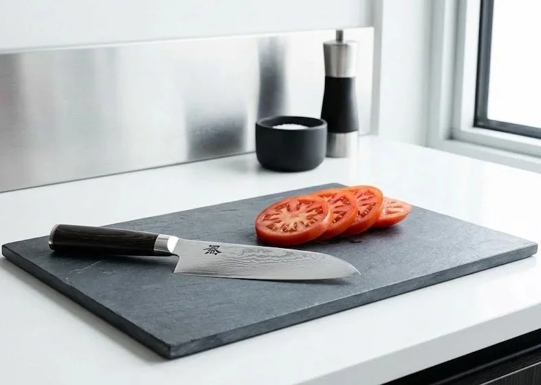 BIFL forged steel chef's knife and sliced tomatoes on a slate prep board—an elevated study in precision kitchen tools.