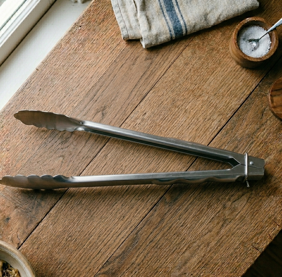 Professional-grade BIFL stainless steel locking tongs on a minimalist surface—a high-tension instrument for precise protein management and the Heirloom Standard.