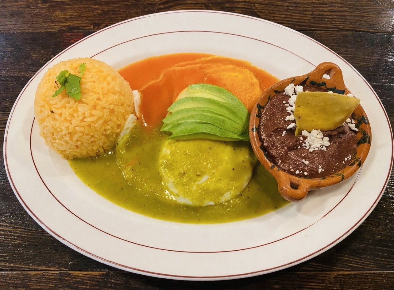 A plate of Mexican food with rice, avocado slices, green sauce, red sauce, refried beans topped with cheese and a taco with beef and cheese.