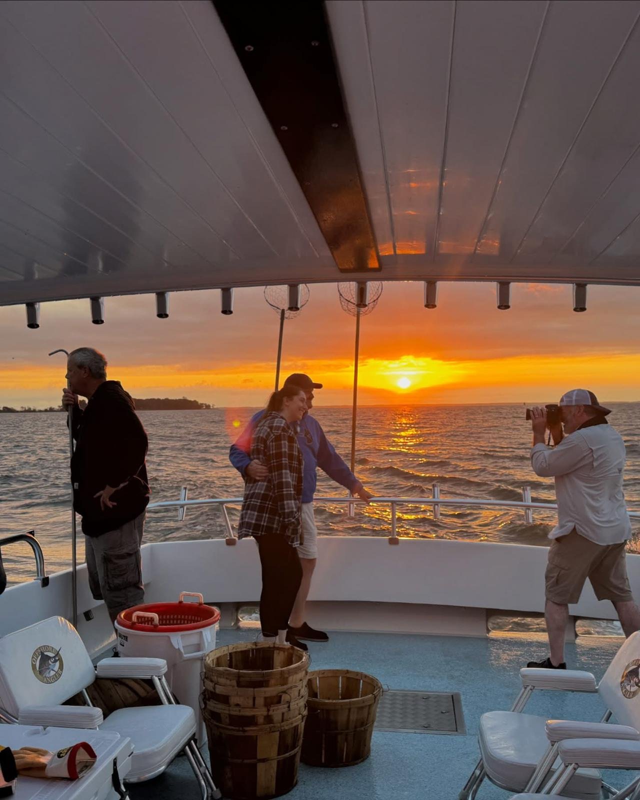 People on a boat at sunset, taking photos and enjoying the view over the water.