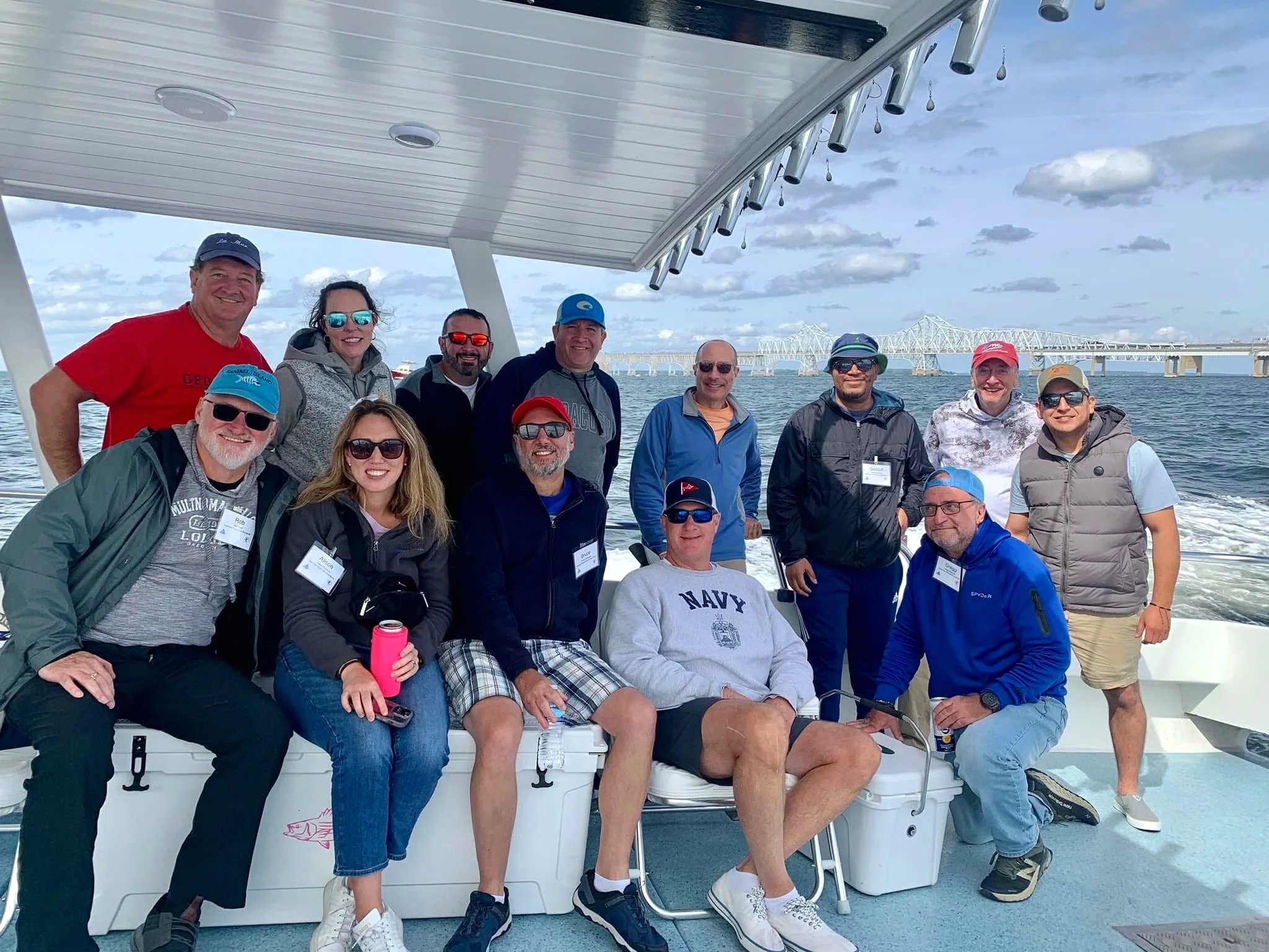 Group of people smiling on a boat with bridge and water in the background.