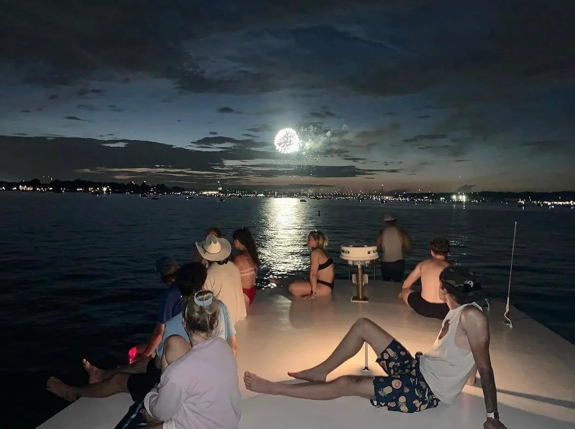 People sitting on a boat at night with a full moon reflecting on the water, enjoying the view and socializing.