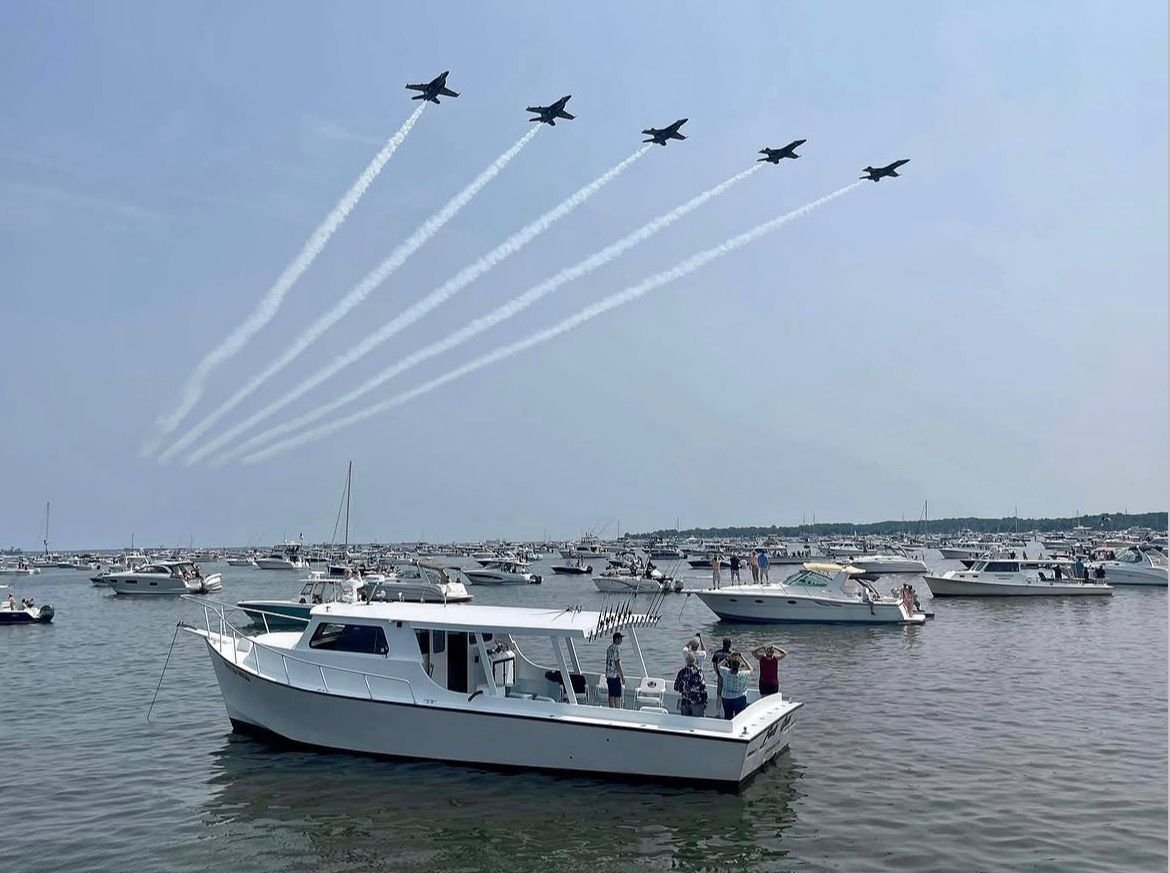 Six fighter jets flying in formation above a marina with boats, creating white smoke trails in the sky.