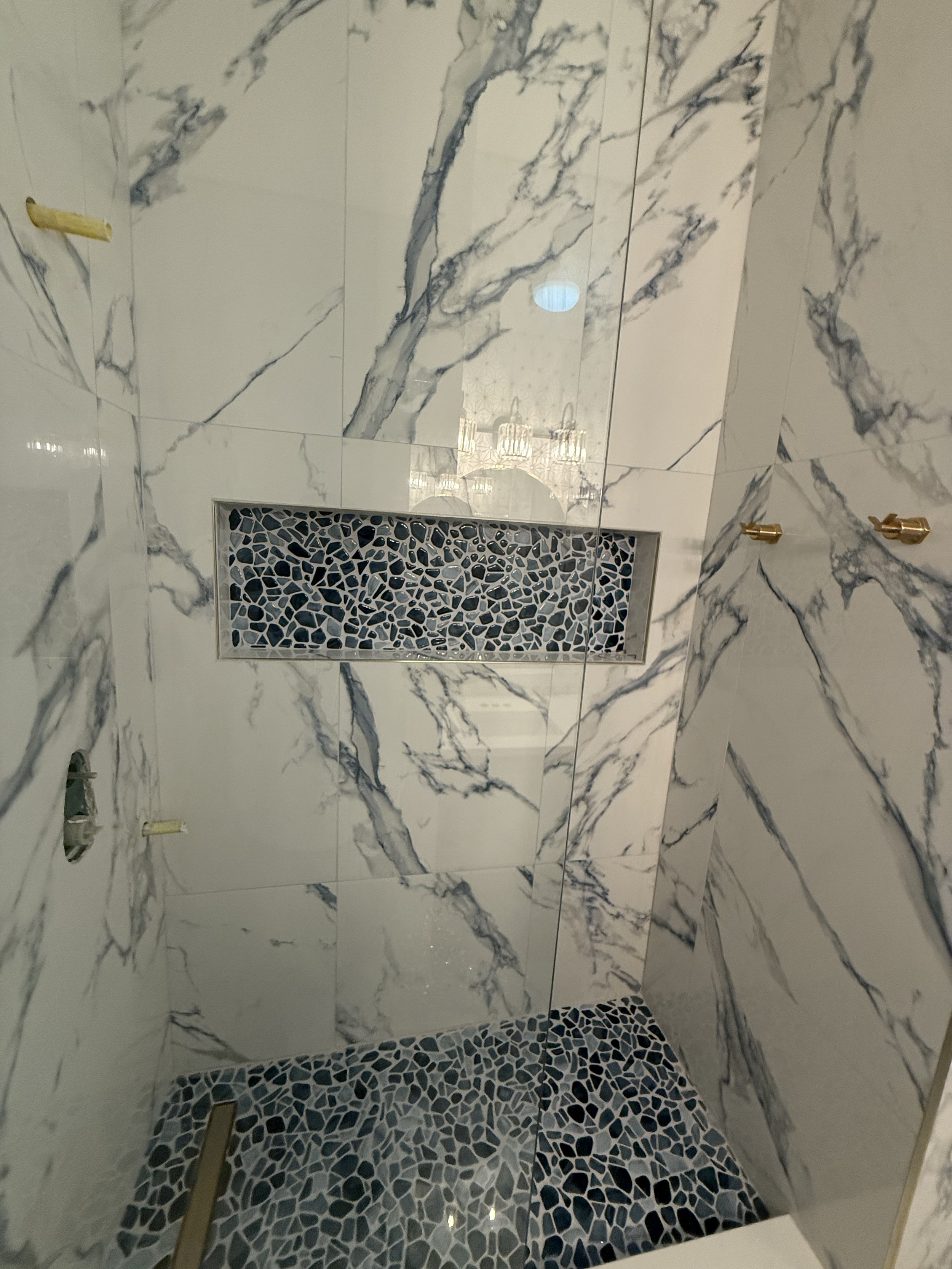 A marble shower with a built-in niche filled with small black and white mosaic tiles and gold fixtures.