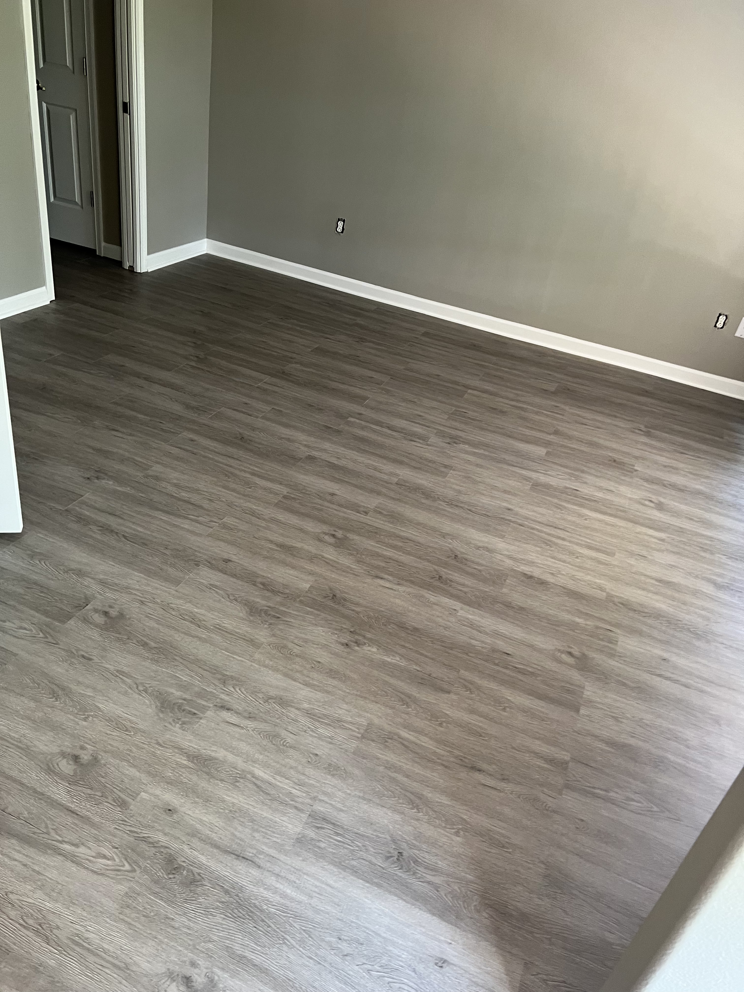 Empty room with gray walls, white baseboards, and wood laminate flooring.