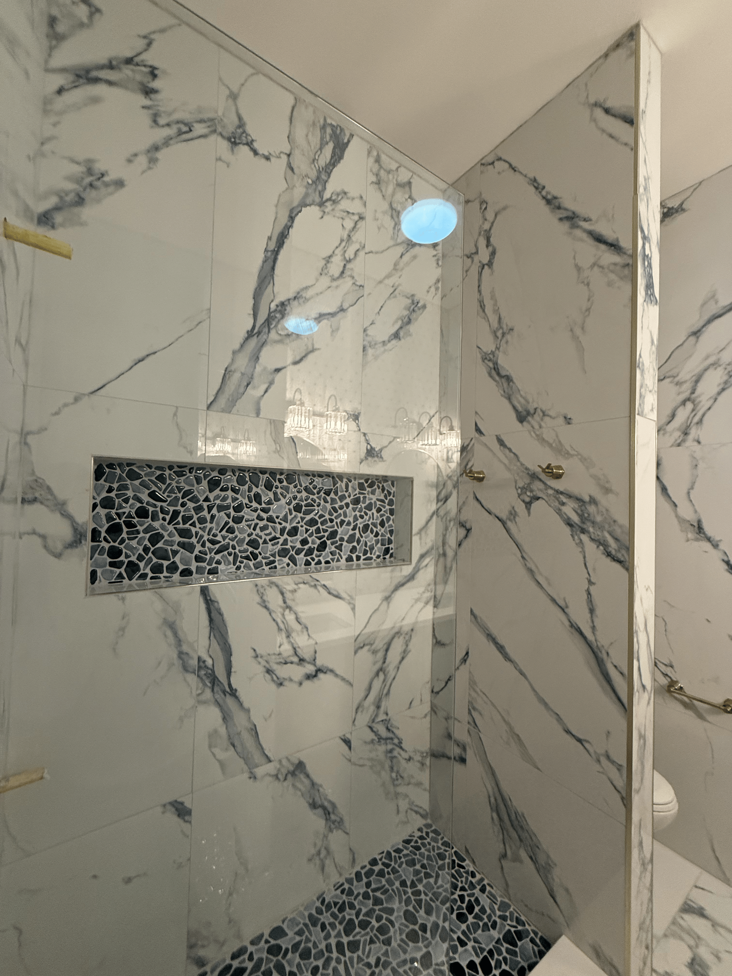 Bathroom interior with marble walls, a tiled shower with dark pebble floor, and a wall mirror.