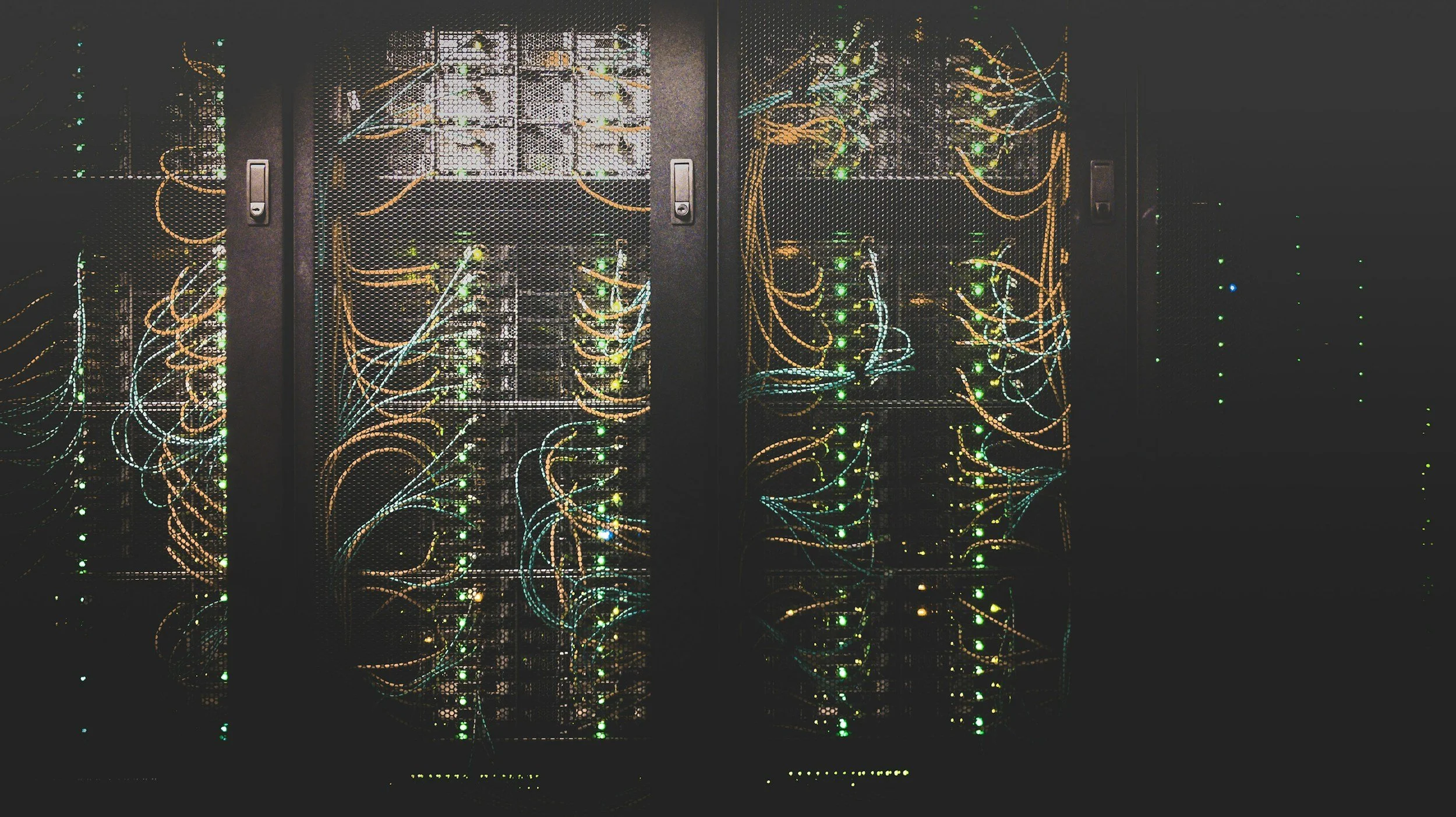 A row of black server racks with blinking green and yellow lights, visible through a perforated metal door.