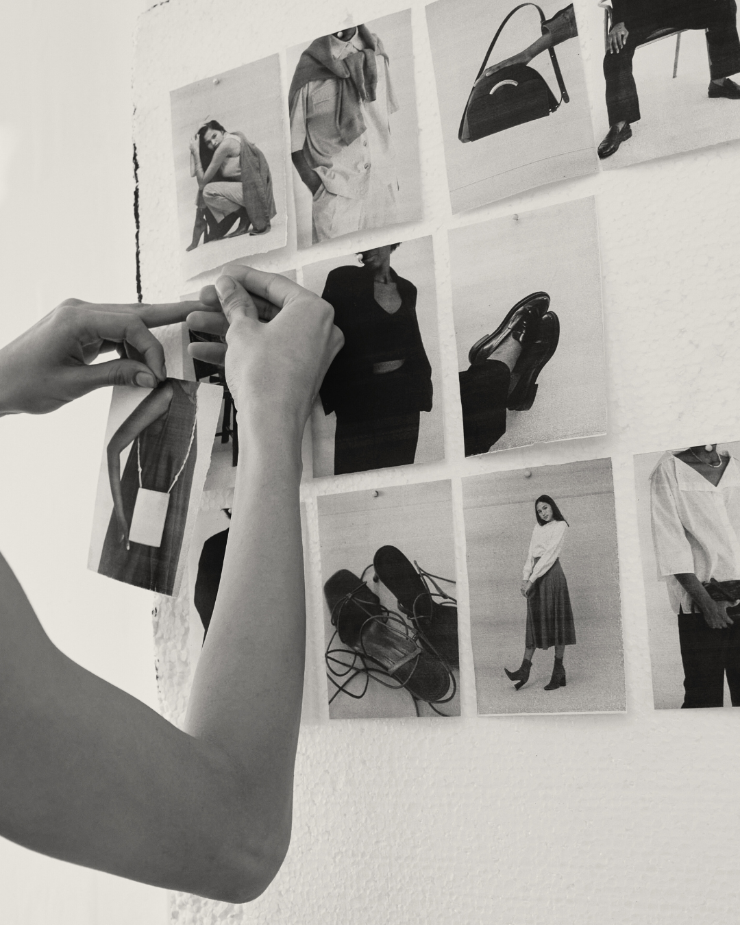 A person hanging a small photograph of clothing onto a wall display of black-and-white fashion photos.