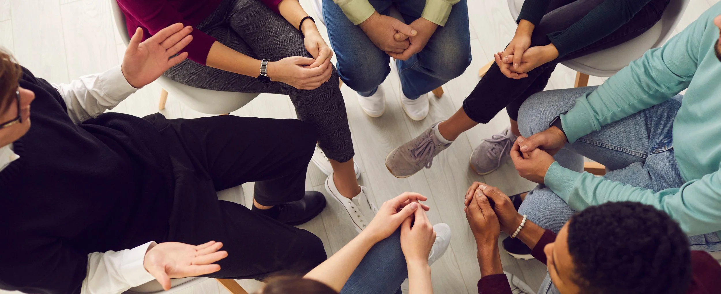 A group of diverse people sitting in a circle, holding hands and engaging in a discussion or support session.