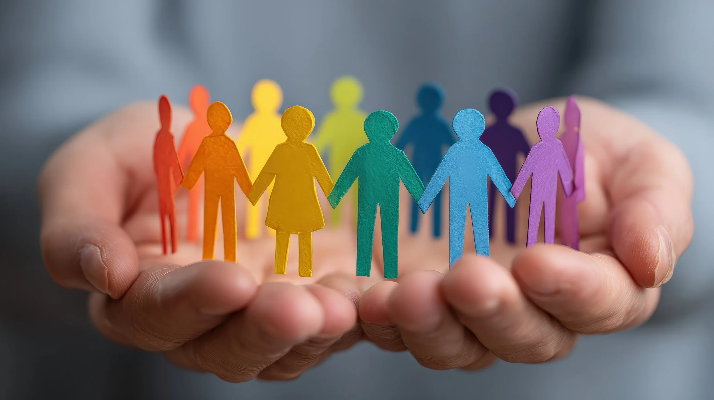 A hand holding colorful paper cutout figures of people arranged in a circle, representing diversity and unity.