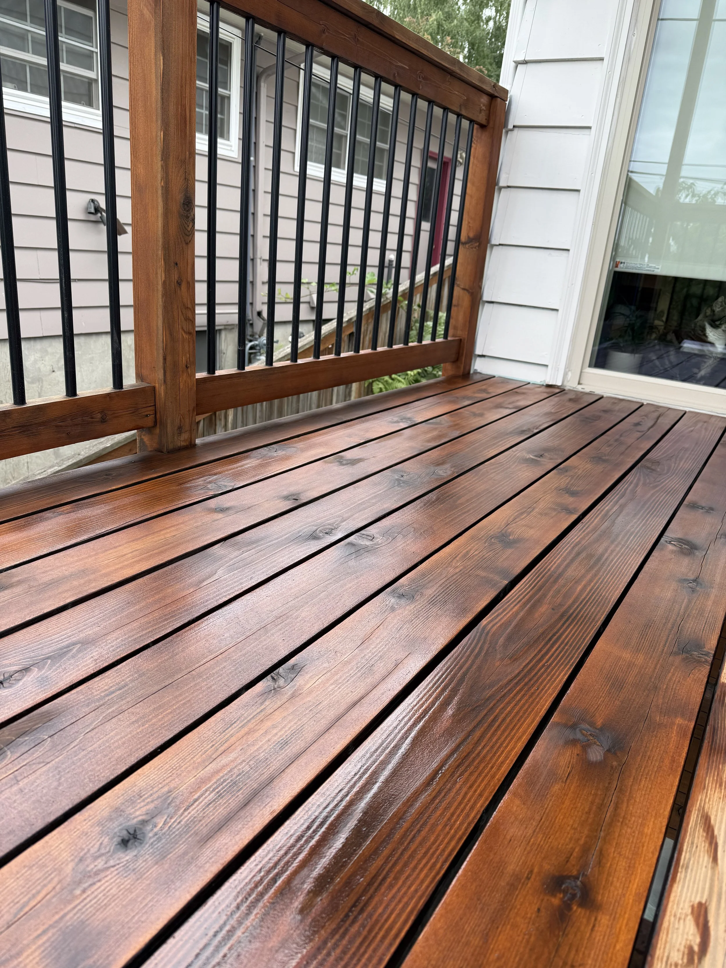 Freshly stained reddish-brown wooden deck with black metal railing on a Beaverton home, exterior deck staining by Cascade Painting