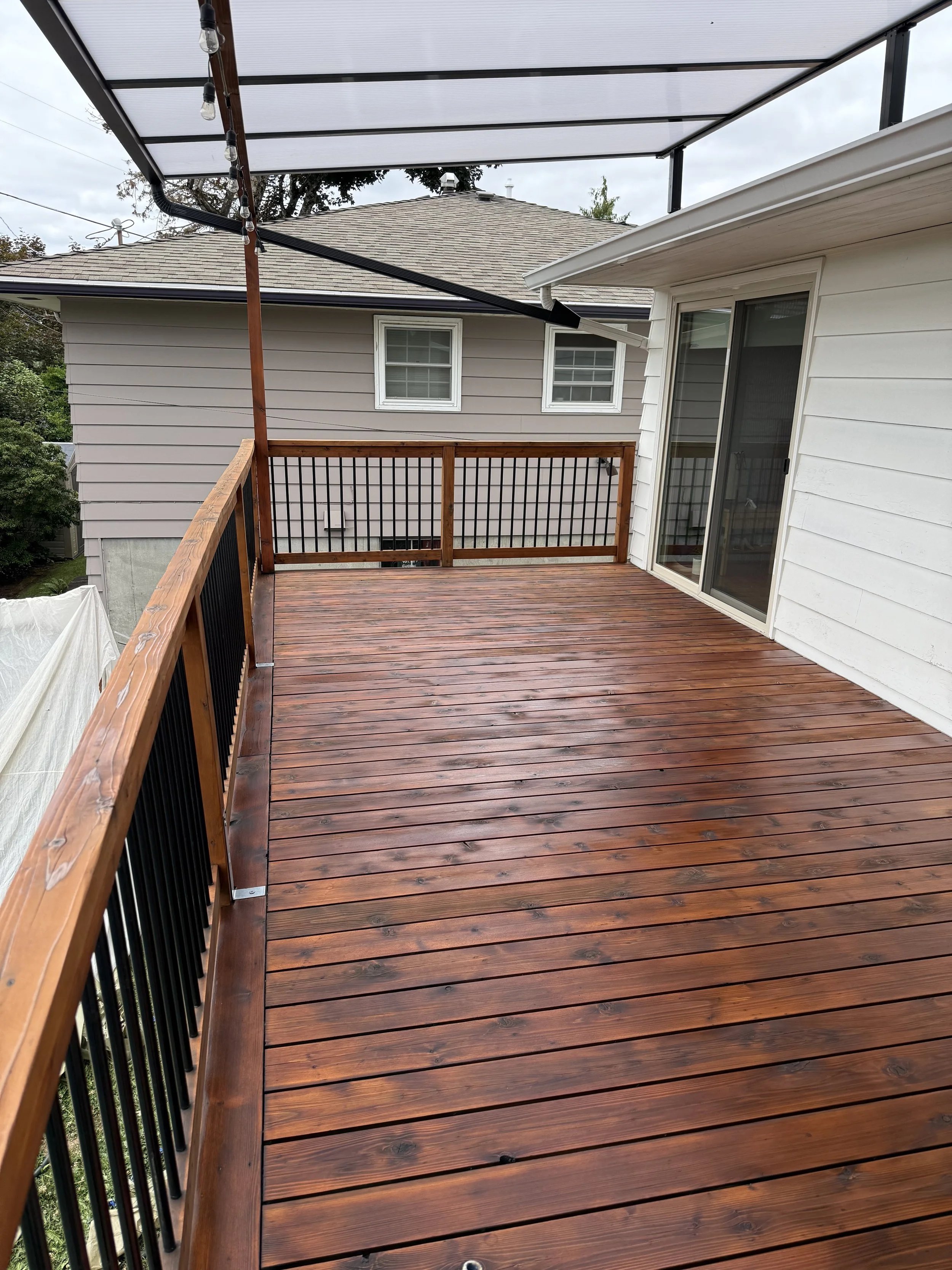 Restained wooden deck with black metal railing on a Beaverton home with painted beige siding, exterior project by Cascade Painting