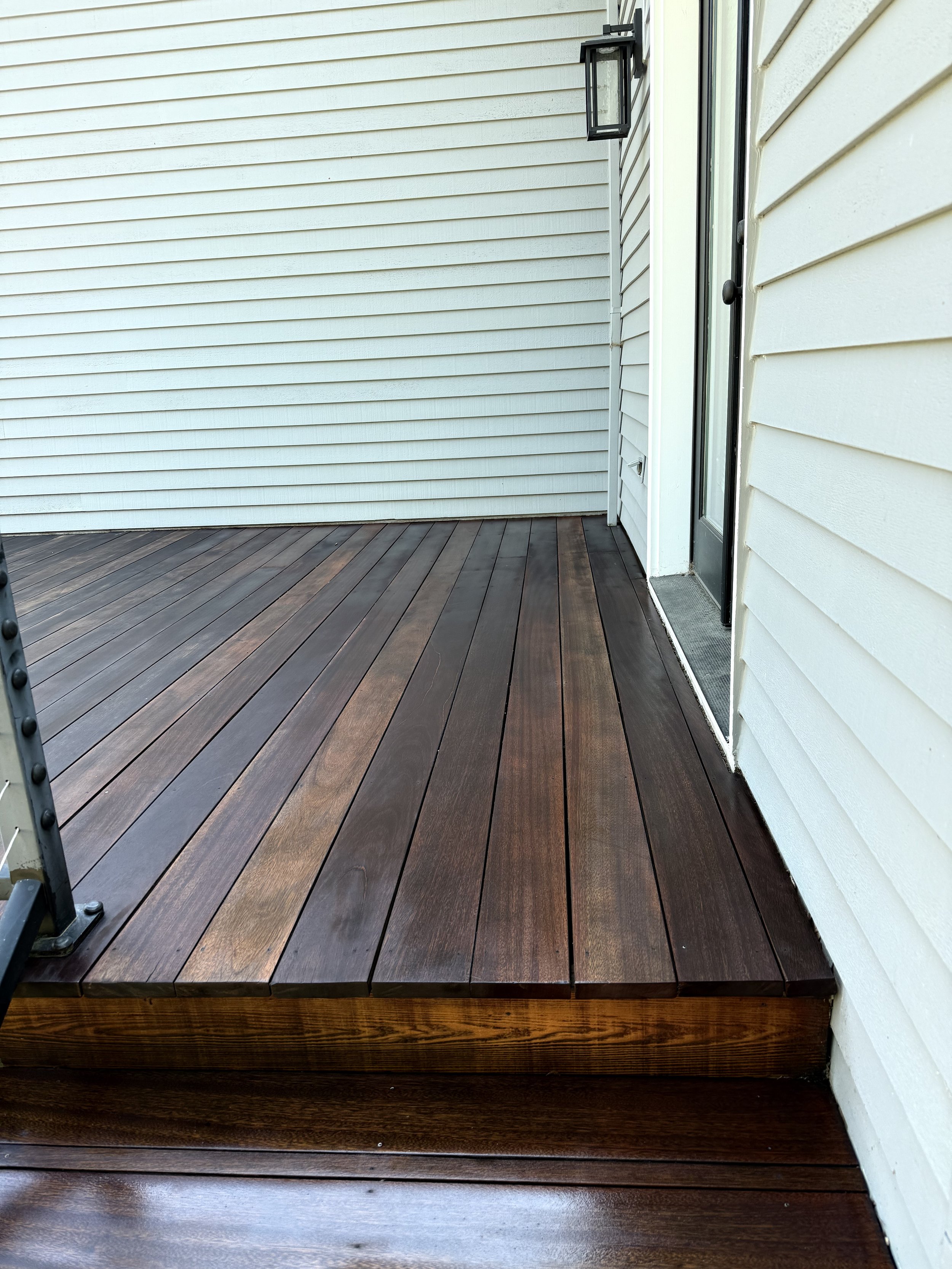 Stained wooden patio deck and step beside a freshly painted white home exterior, Cascade Painting project in Westside Portland