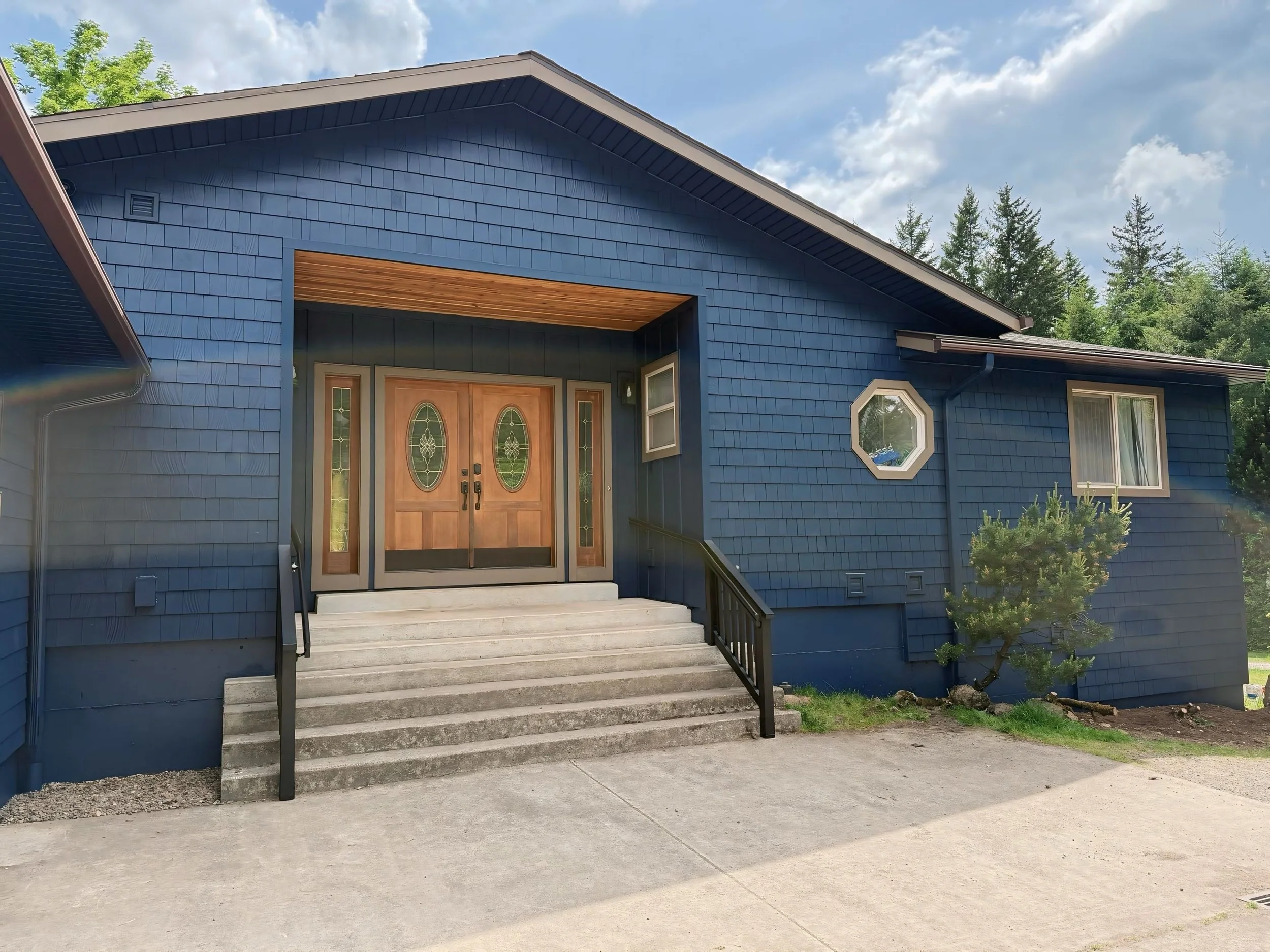 Freshly painted blue home in Beaverton with stained wooden double door and detailed exterior trim by Cascade Painting