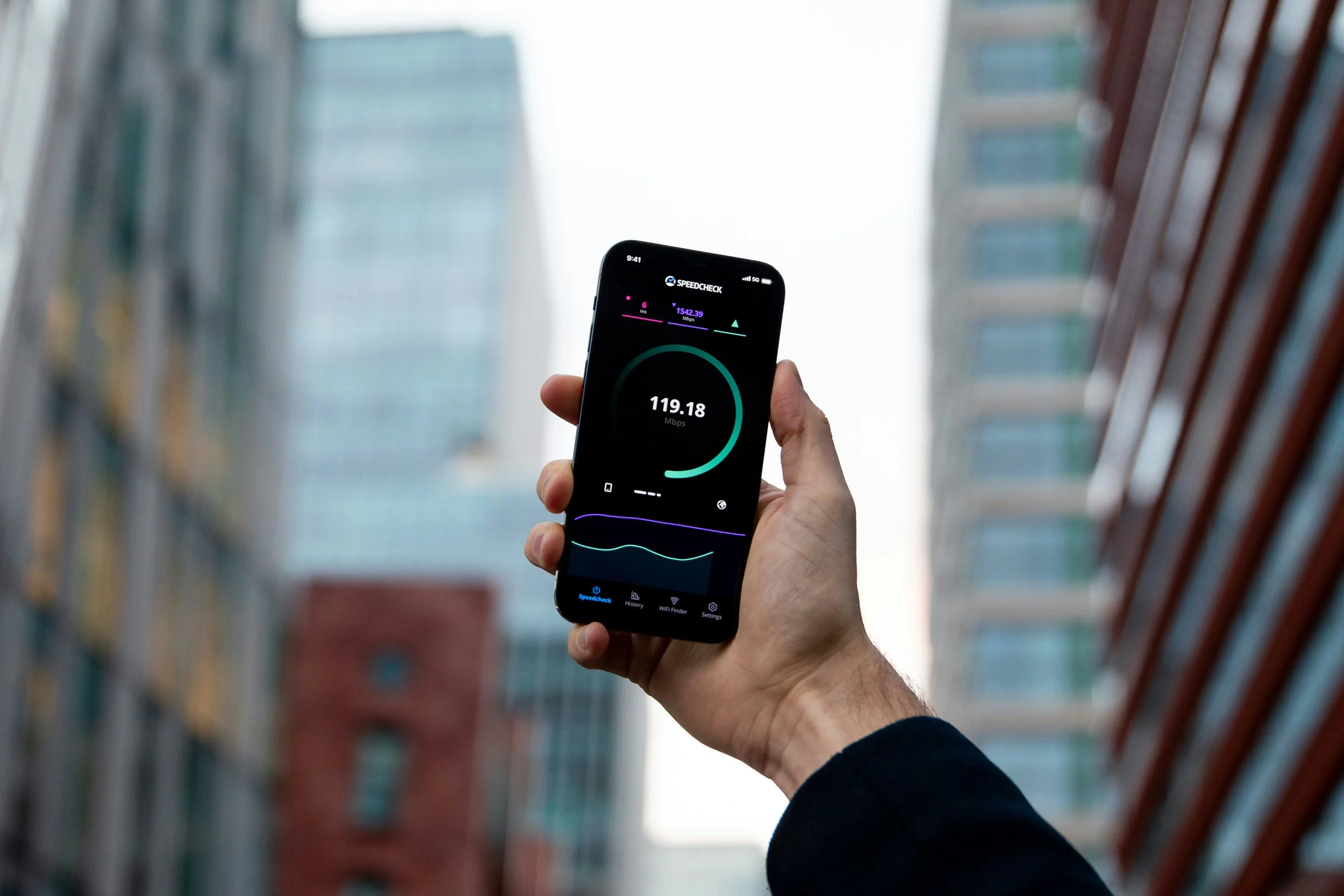 A person holding a smartphone displaying an internet speed test result of 119.18 Mbps in a library aisle with blurred books on shelves.