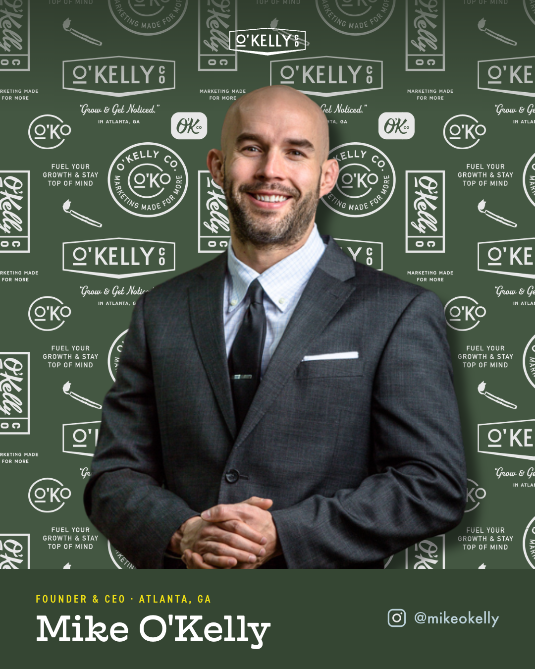 Professional man in a dark suit, white shirt, and black tie smiling, standing in front of a green backdrop with logos and text about O'Kelly Co, Atlanta, Georgia, promoting growth and marketing.