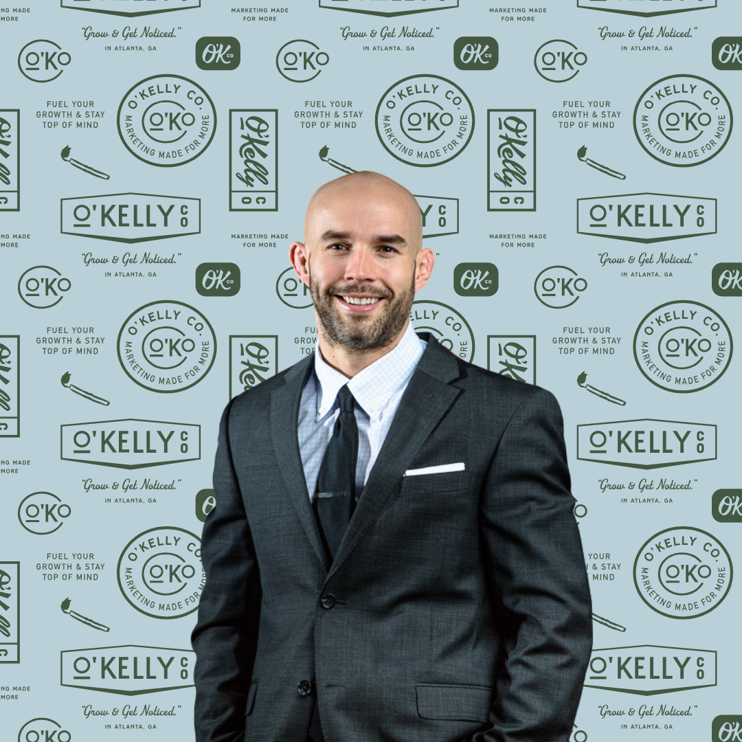 Mike O'Kelly, Founder and CEO of O'Kelly Co., in a suit against a background of O'Kelly Co. logos
