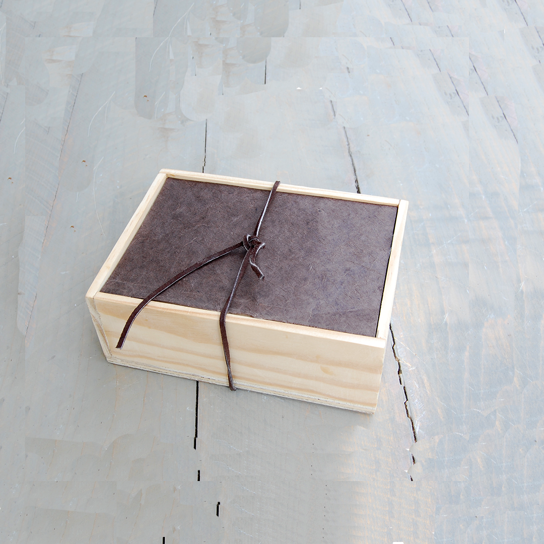 A wooden box with a dark lid tied with a black string on a light wooden surface.