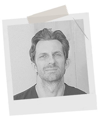 Black-and-white photo of a man with short hair and a beard, looking at the camera.