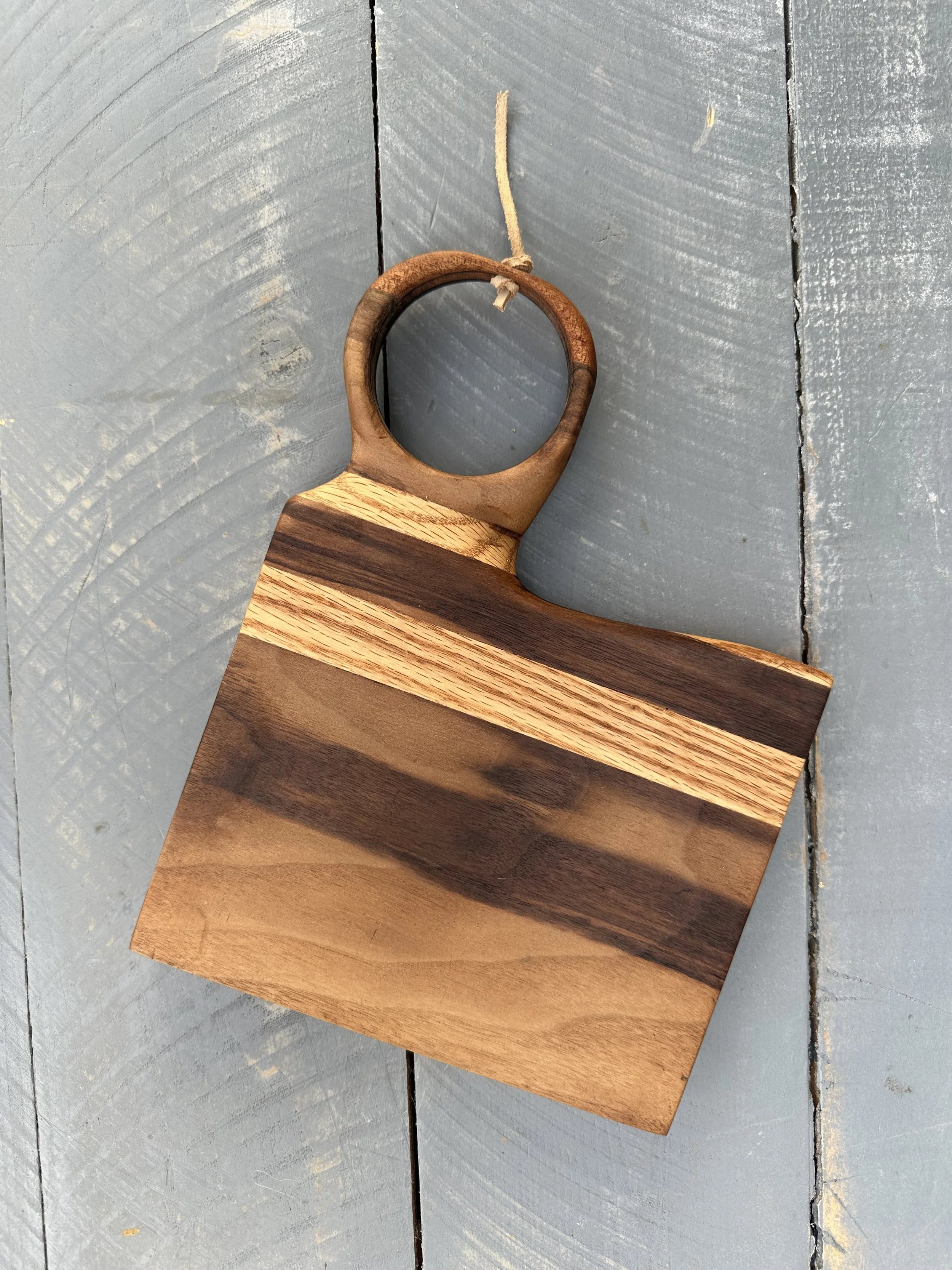 A wooden cutting board with horizontal dark and light wood stripes, placed on a gray wooden surface.