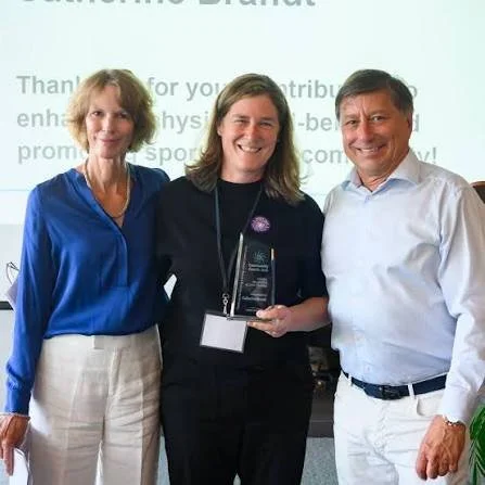 Three people standing together with one holding an award, smiling at an event or presentation.