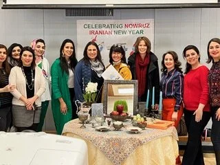 Group of women standing behind a table with food and decorations at an event celebrating Nowruz and New Year