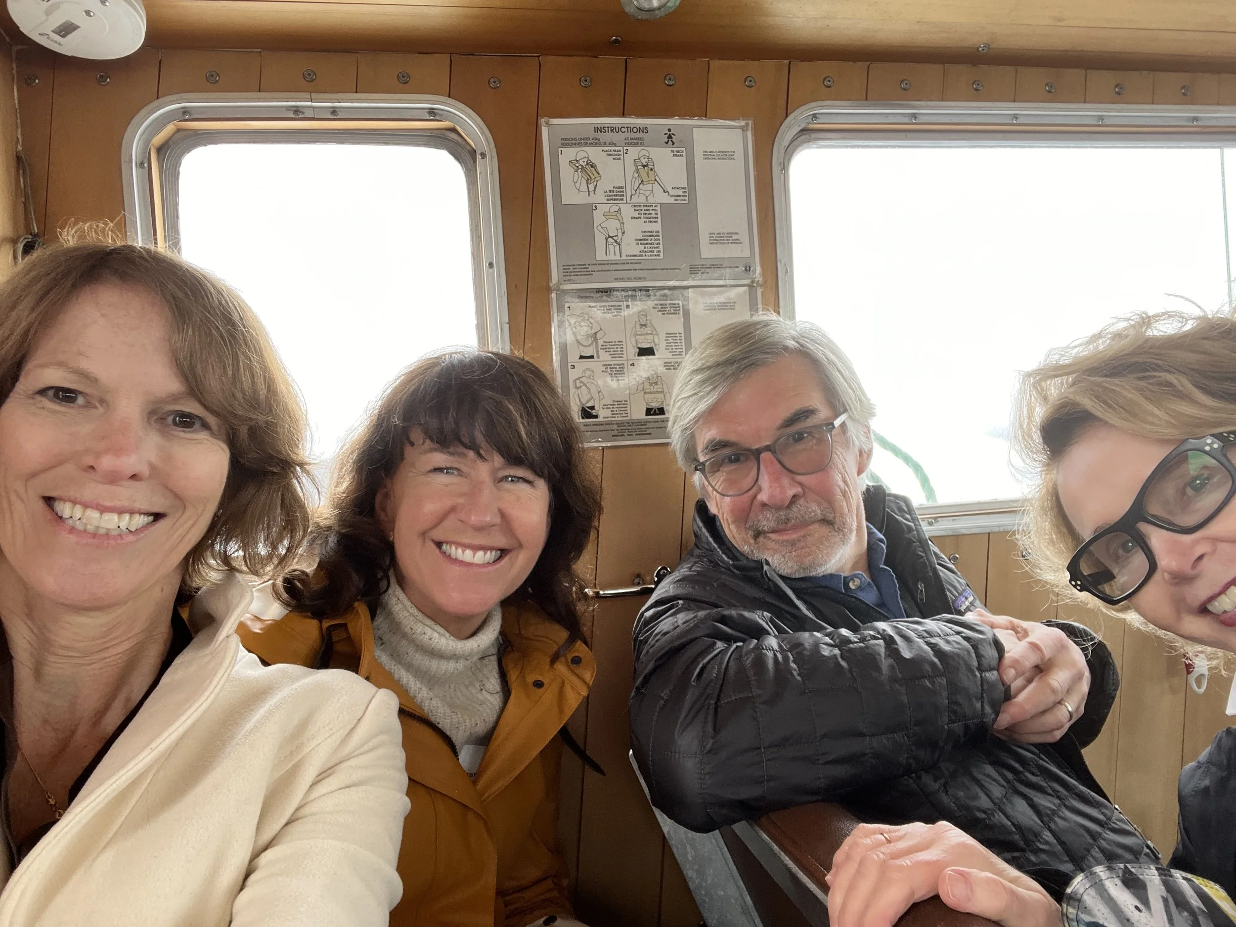 A group of five smiling people taking a selfie inside a wooden-paneled room with bright windows. The top center of the wall has instructions and diagrams for safety procedures.