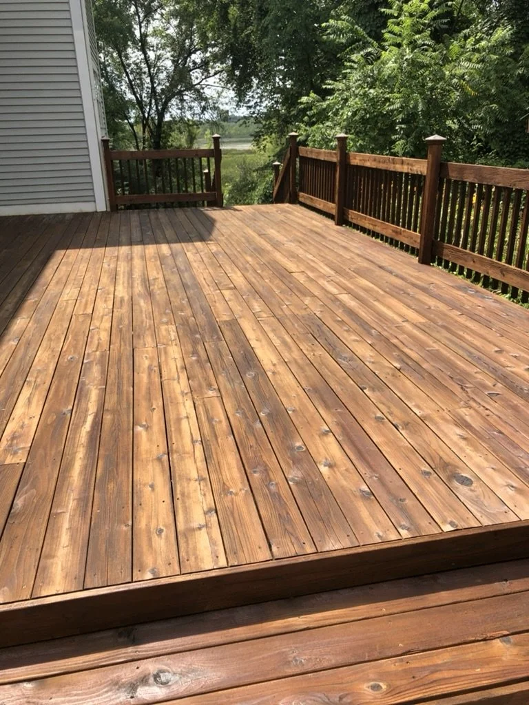 Wooden deck with railing overlooking a backyard with trees.