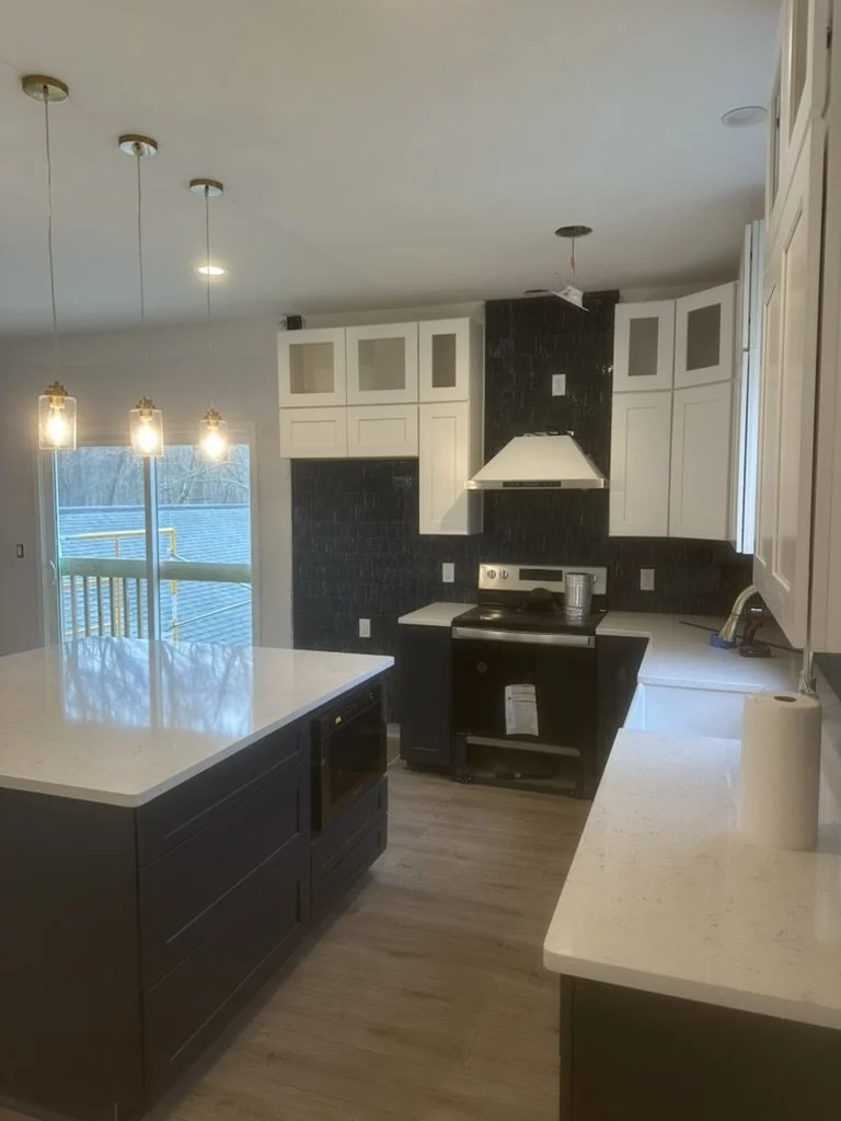 Kitchen with white and black cabinets, countertops, and modern pendant lighting, with a sliding glass door leading outside.