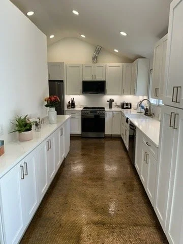 Modern kitchen with white cabinetry, black appliances, and hardwood floors. Potted plants on the left counter and kitchen utensils near the sink.