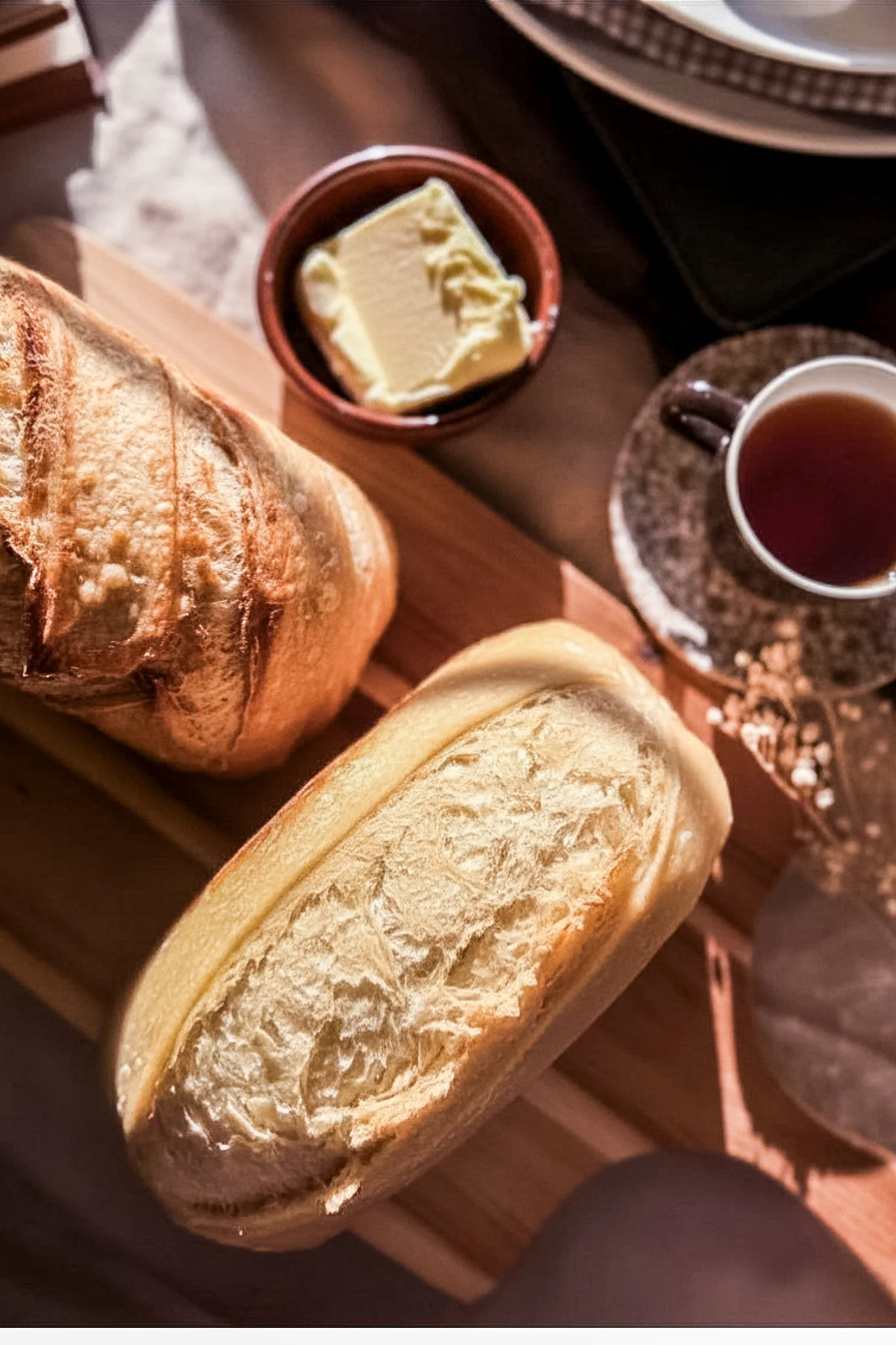 Close-up of sliced bread, a small dish of butter, coffee cup on a saucer, and a turntable in the background.