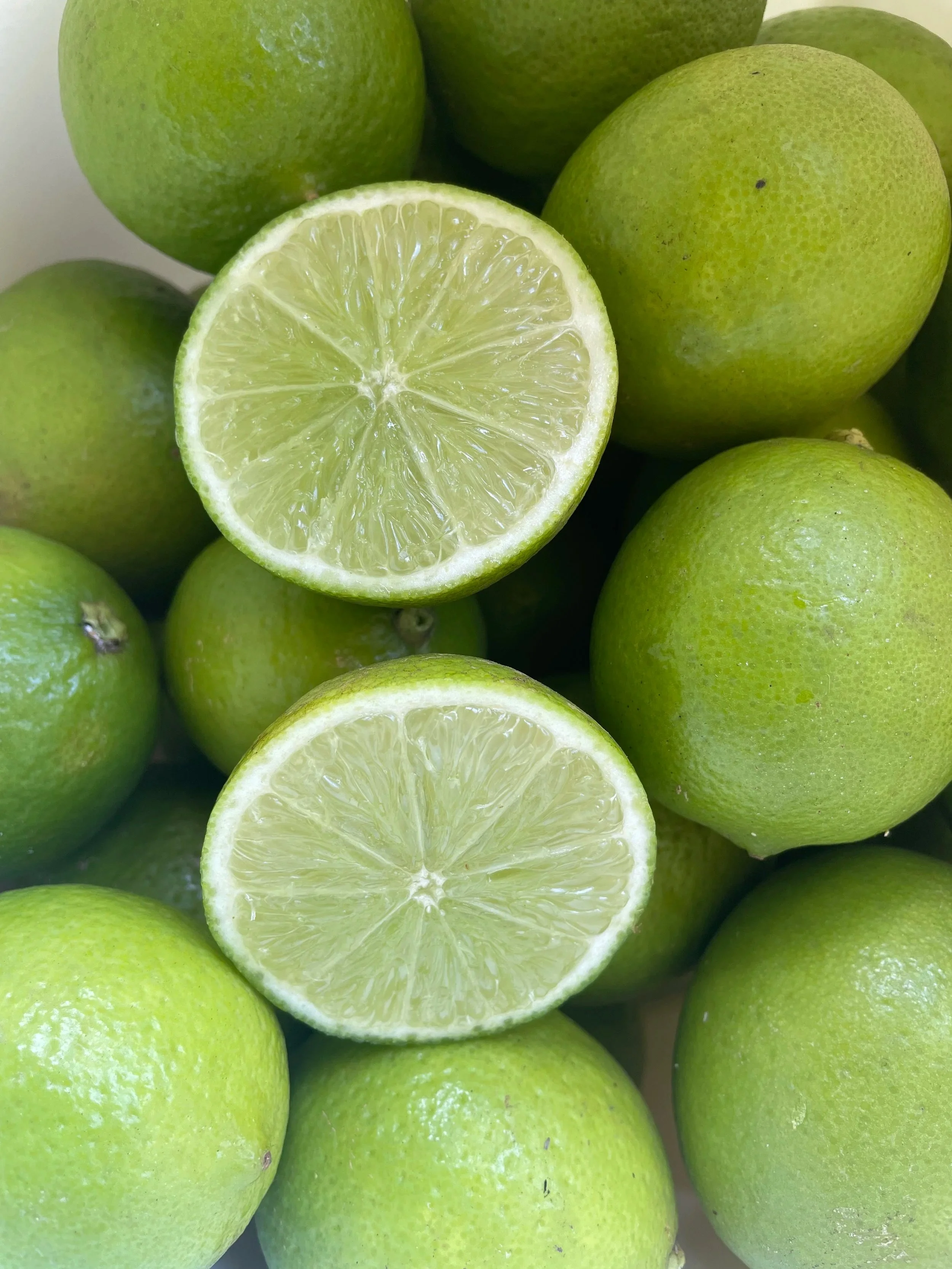 Close-up of several green limes, with one lime cut in half showing the juicy, segmented interior.