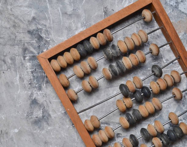 A vintage wooden abacus with alternating light and dark beads on metal rods, placed on a textured gray surface.