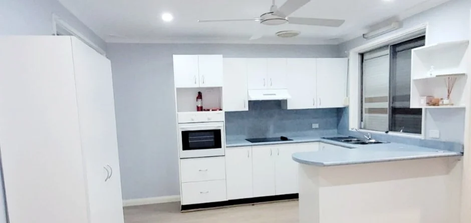 Modern kitchen with white cabinets, gray countertop, built-in microwave, stovetop, sink, window, and open shelving