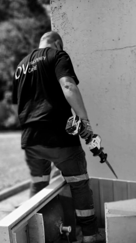 A worker in uniform holding a power drill, standing in an outdoor construction or maintenance area.