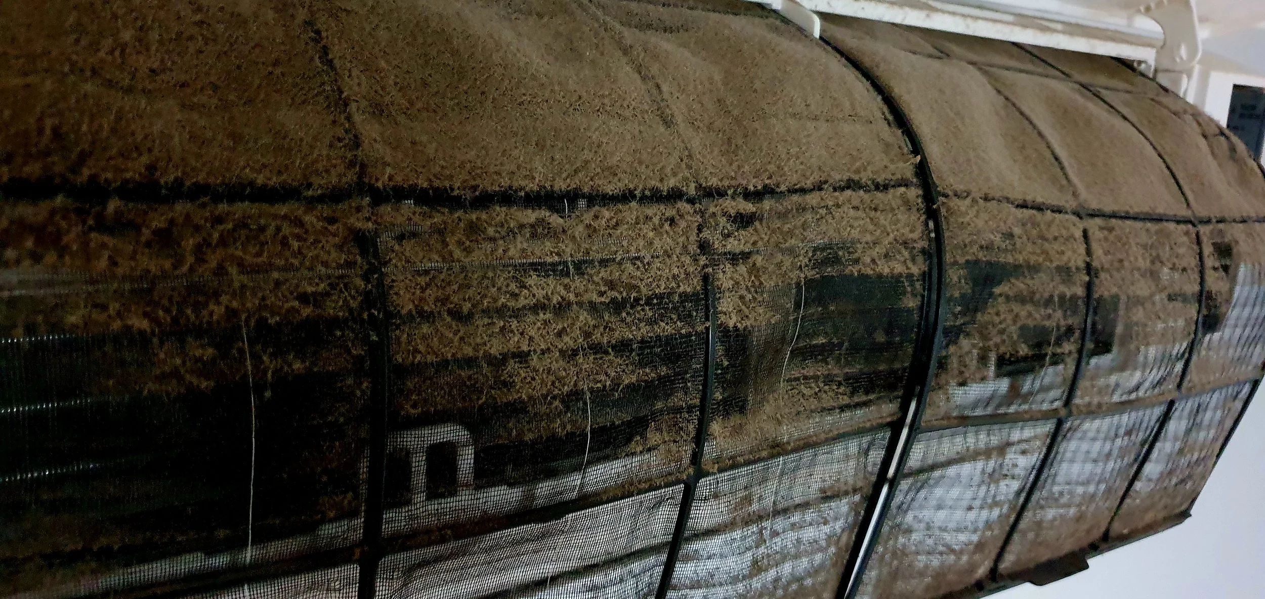 A close-up of a large, cylindrical farming structure covered in brown, textured fabric with black wire framing.