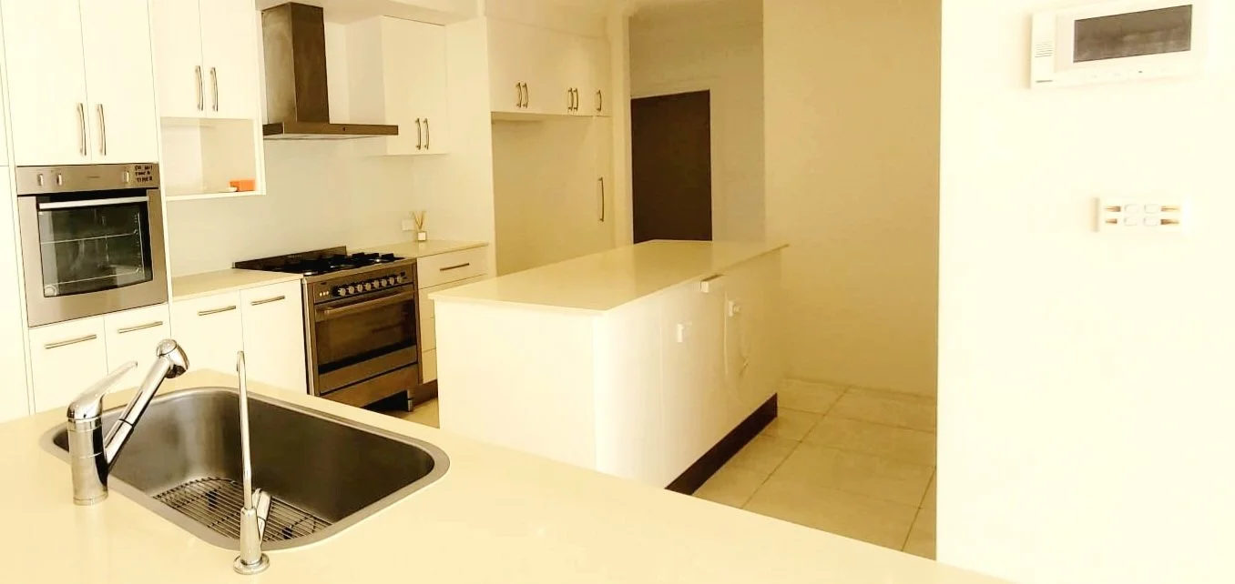 Modern kitchen with white cabinets, a stainless steel oven, a gas stove, a built-in microwave, and a double sink with a faucet, with beige tiled flooring and an air conditioning unit on the wall.