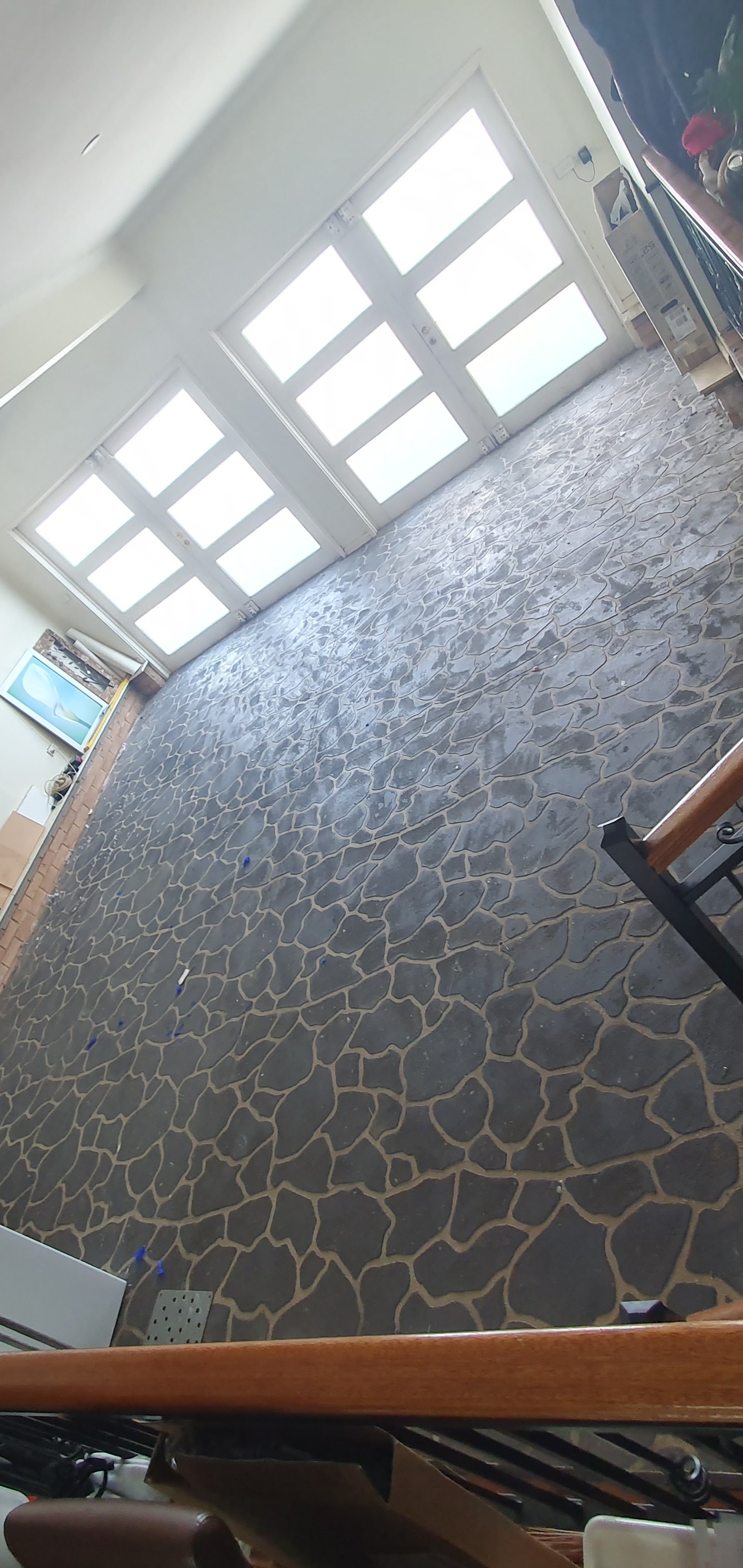 A room with black stamped concrete flooring, white walls, large front door with glass panels, and a television mounted on the left wall.