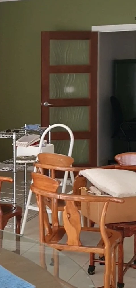 A room with a partially open wooden door with frosted glass panels, a white high chair, and a wooden armchair with a cushion, all in front of green and gray walls.