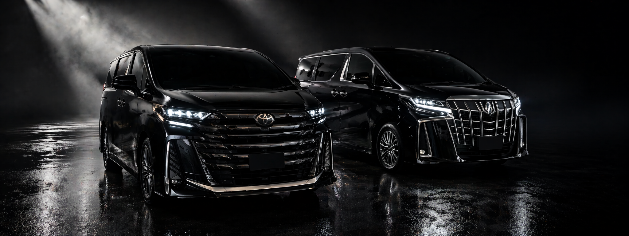 Two black luxury minivans parked indoors on a reflective wet floor, illuminated by spotlights with a dark background.