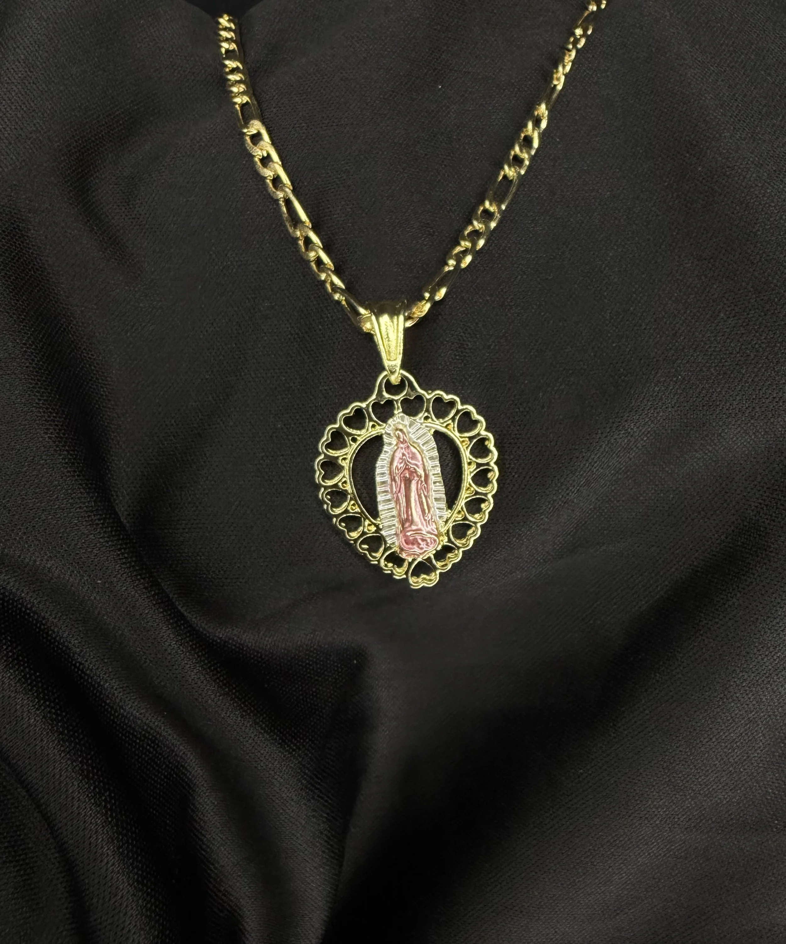 A gold chain necklace with a pendant that features an image of the Virgin of Guadalupe, set against a black fabric background.