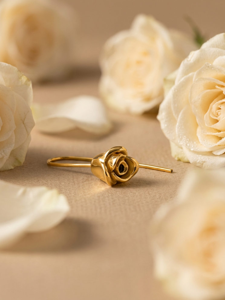 Gold ring with a rose-shaped design surrounded by white roses and scattered rose petals on a neutral background.