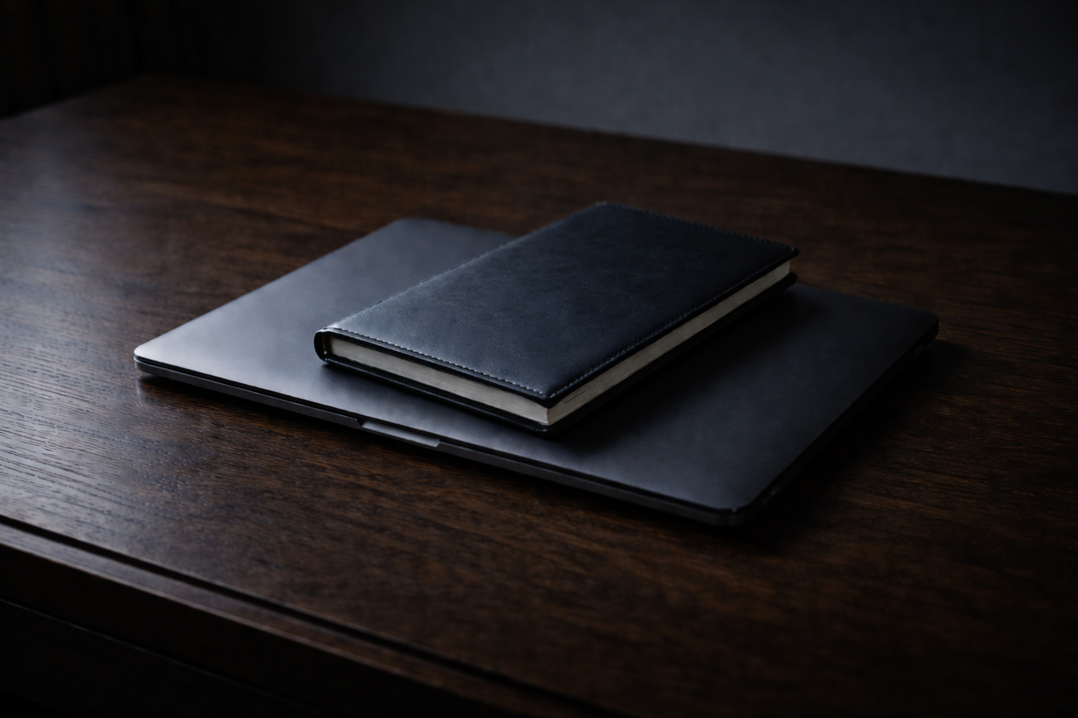 A closed black laptop, a black notebook, and a black wallet resting on a dark wooden surface. Symbolic image representing compulsive sexual behavior, a behavioral addiction treated at Lazar Clinical.