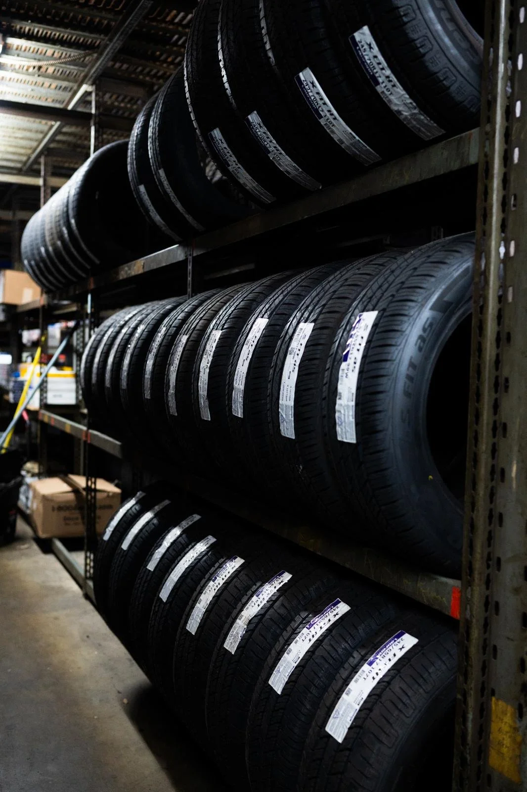 A storage rack holding multiple black car tires with white labels in a warehouse or garage.