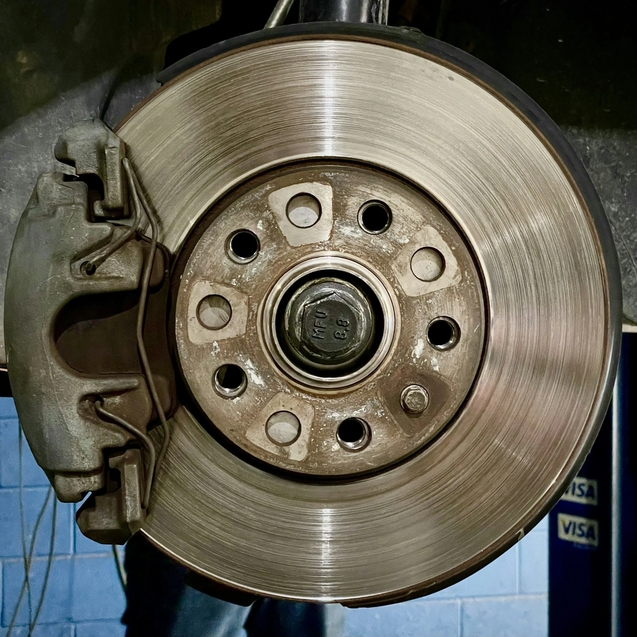 Close-up of a vehicle brake disc with an attached brake caliper, showing metal surfaces with some rust and debris.