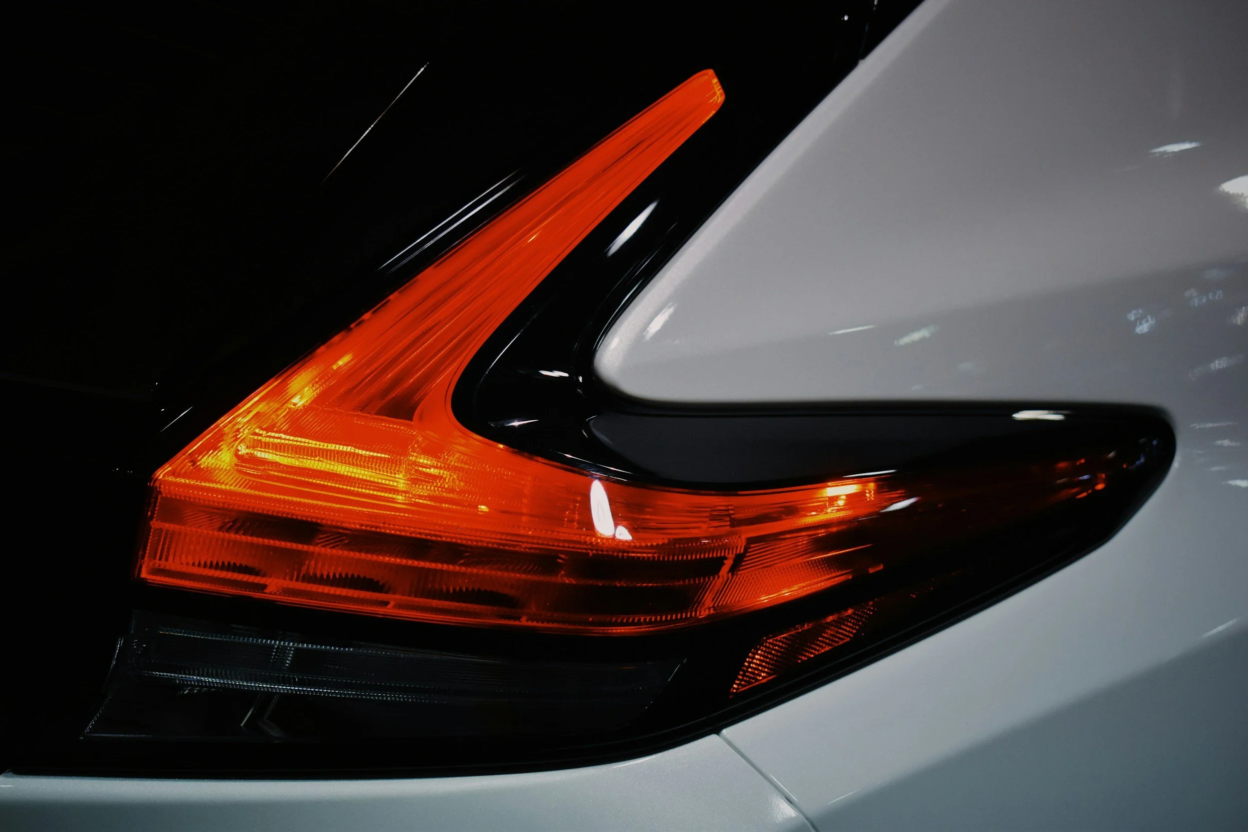 Close-up of a car's rear light with red and orange sections, partially visible with a silver body and dark background.